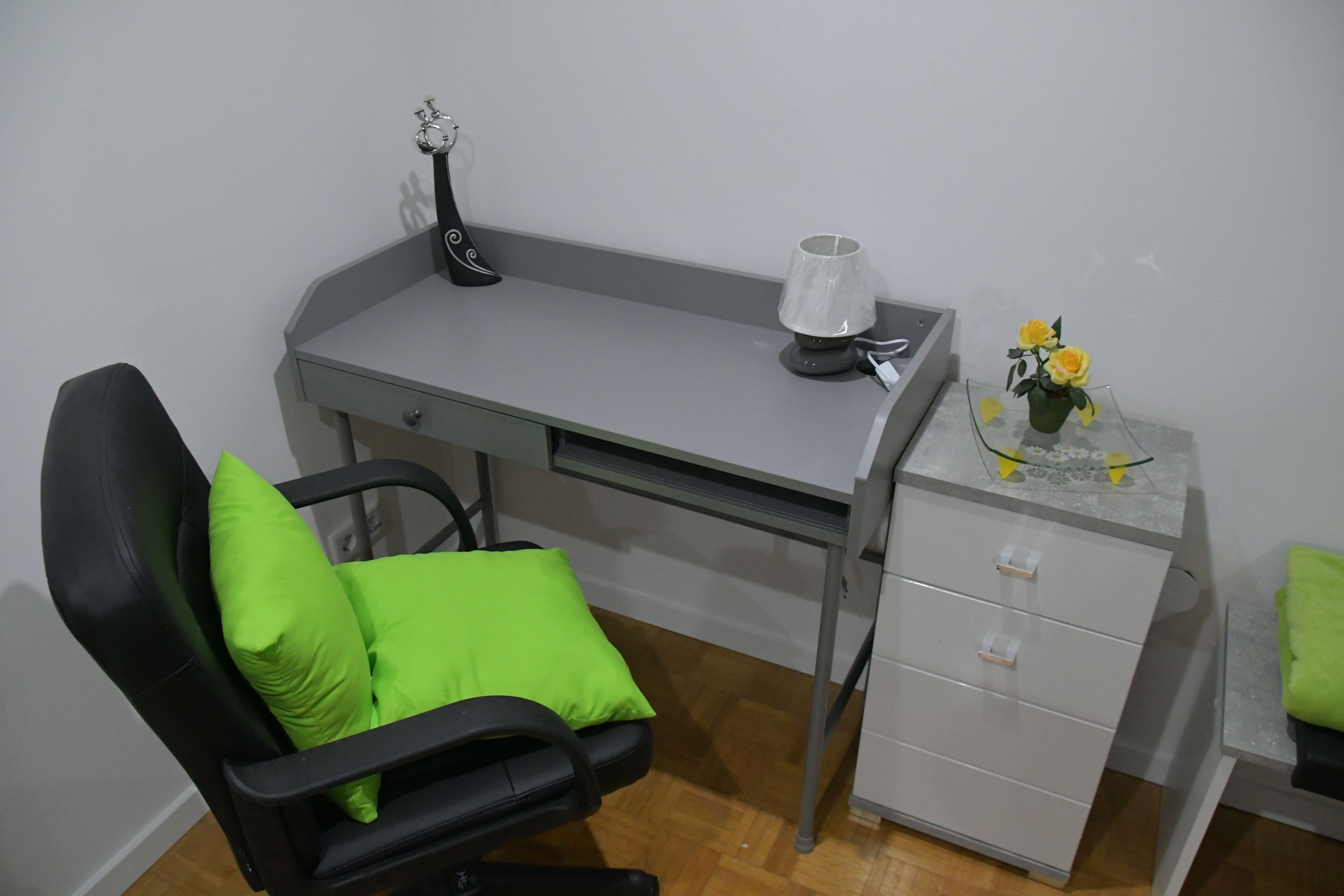 Una oficina pequeña con un escritorio, una silla y un mueble bajo.
