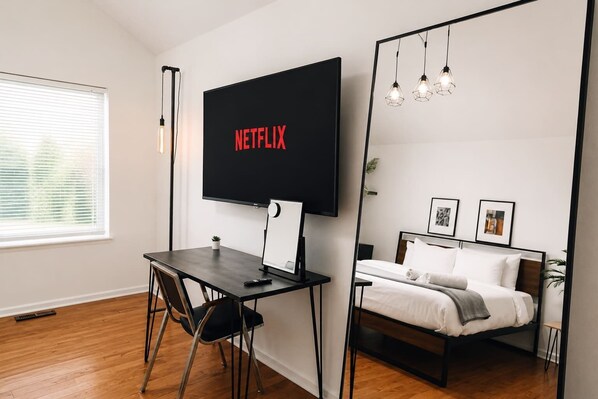 Une chambre d’hôtel moderne équipée d’un grand téléviseur à écran plat, d’un bureau avec une chaise, d’un lit avec une tête de lit et d’un miroir.