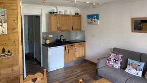 Une cuisine moderne avec des meubles en bois, un lave-vaisselle et un plan de travail. On y trouve un canapé gris avec des coussins à motifs et une table basse en bois.