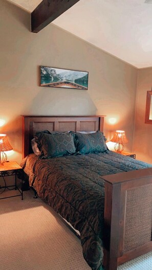 A bedroom with a wooden headboard, a bed with patterned bedding, two bedside lamps, and a framed picture on the wall. - Hideaway in The Blue Mountains ***all seasons*** (The Blue Mountains)