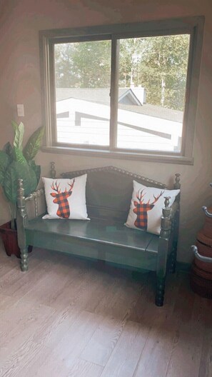 A wooden bench with two white pillows featuring a red and black checkered deer design, positioned in front of a window overlooking a residential area. - Hideaway in The Blue Mountains ***all seasons*** (The Blue Mountains)