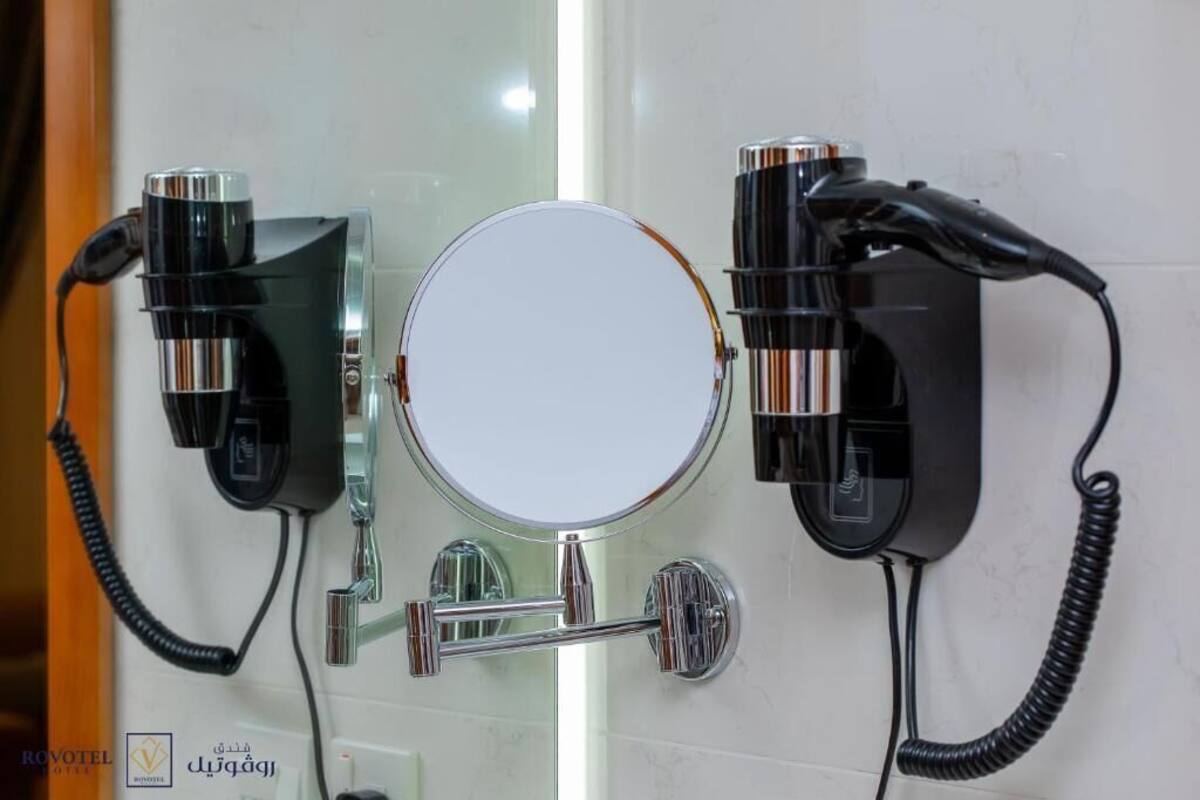 Une salle de bain avec un miroir rond, deux sèche-cheveux et un porte-serviettes.