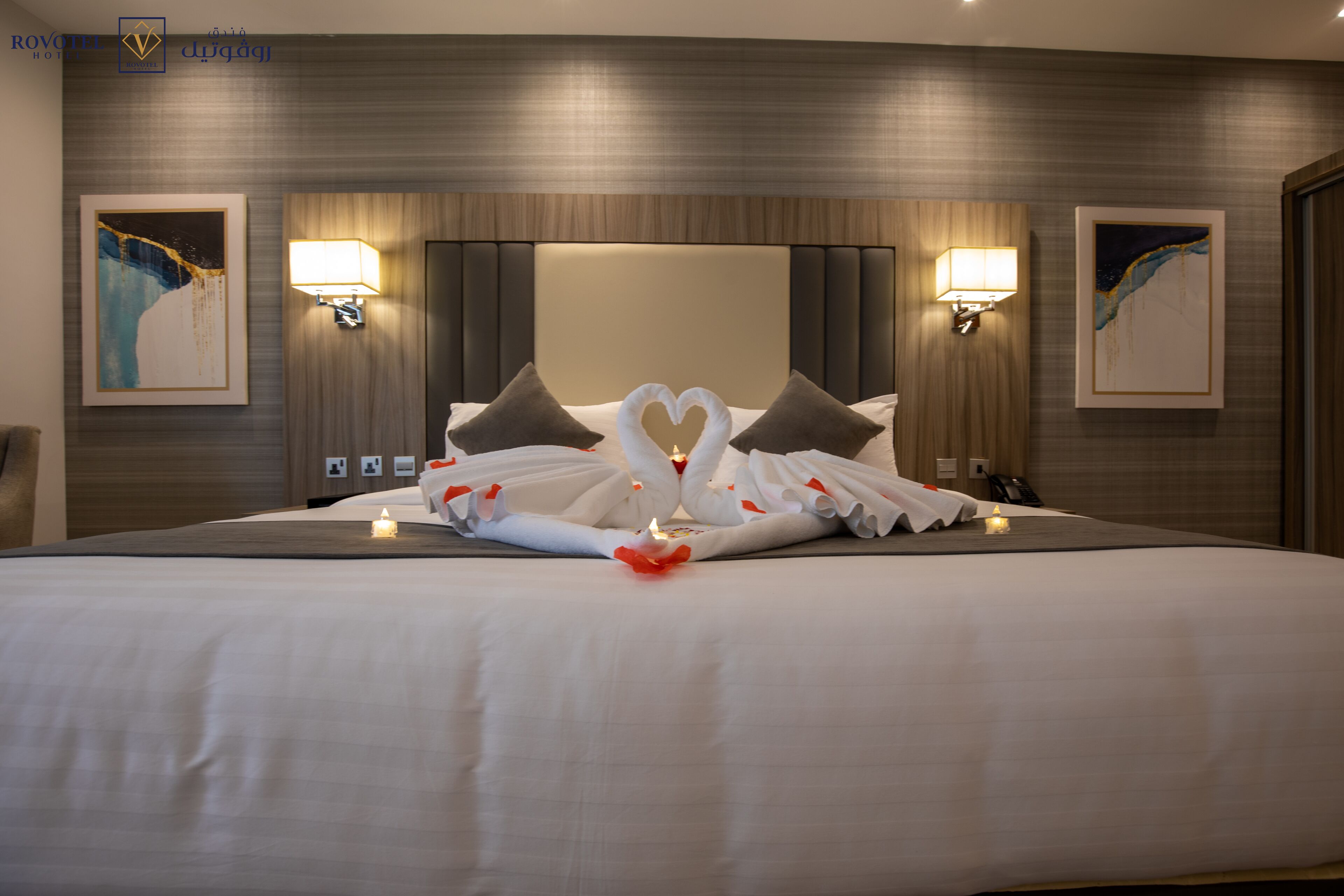 A hotel room with a large bed, two wall-mounted lamps, and two framed artworks.