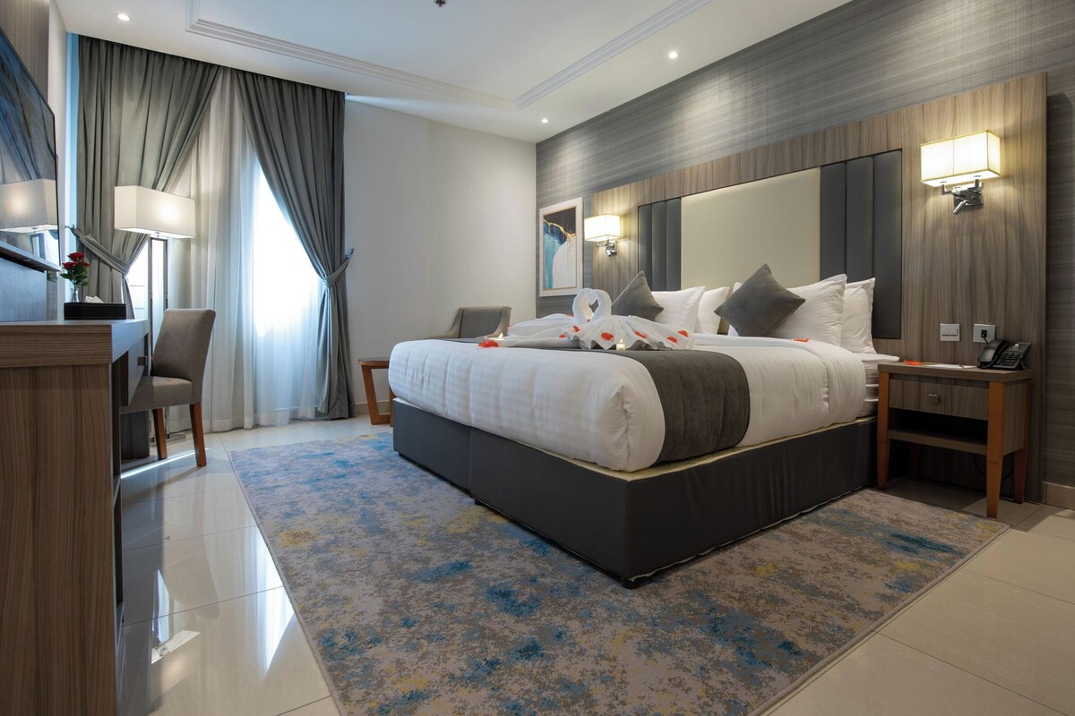 A modern hotel room with a large bed, bedside tables, a desk, and a mirror.