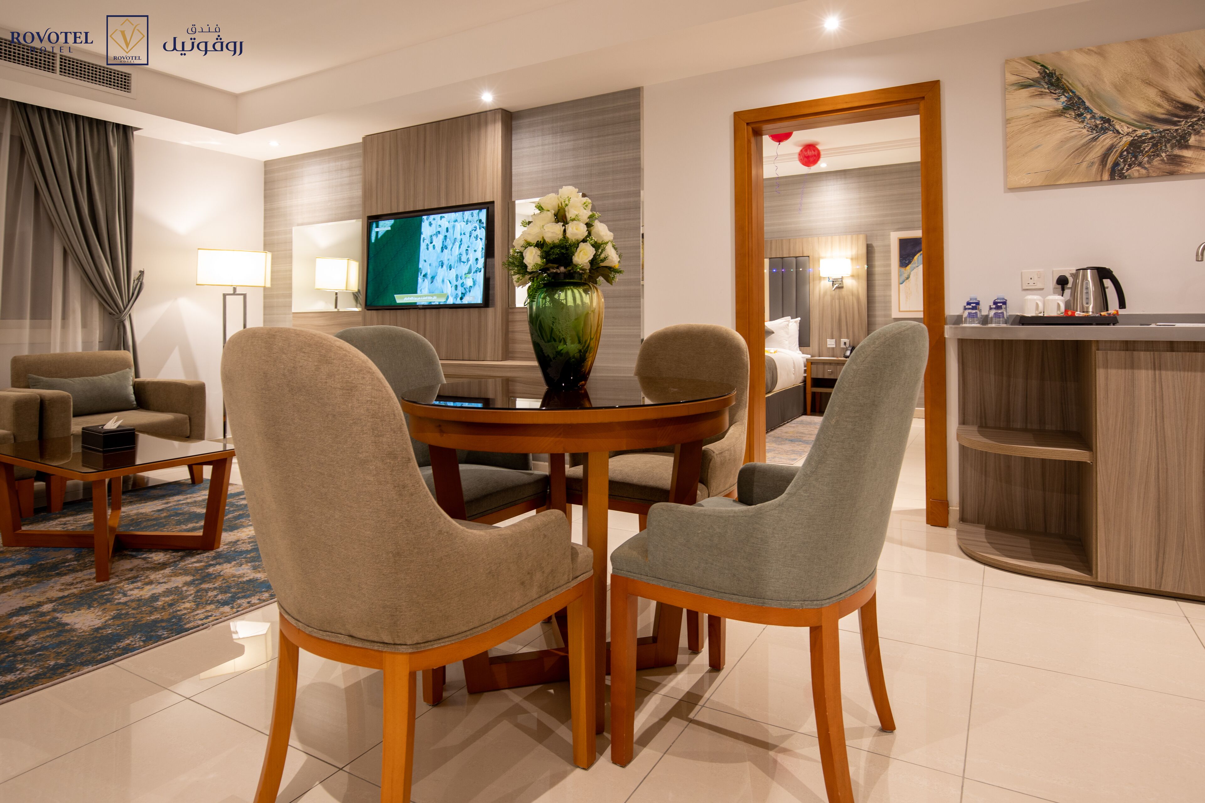 Habitación de hotel moderna con comedor, televisión, un jarrón de flores y zona de cocina.