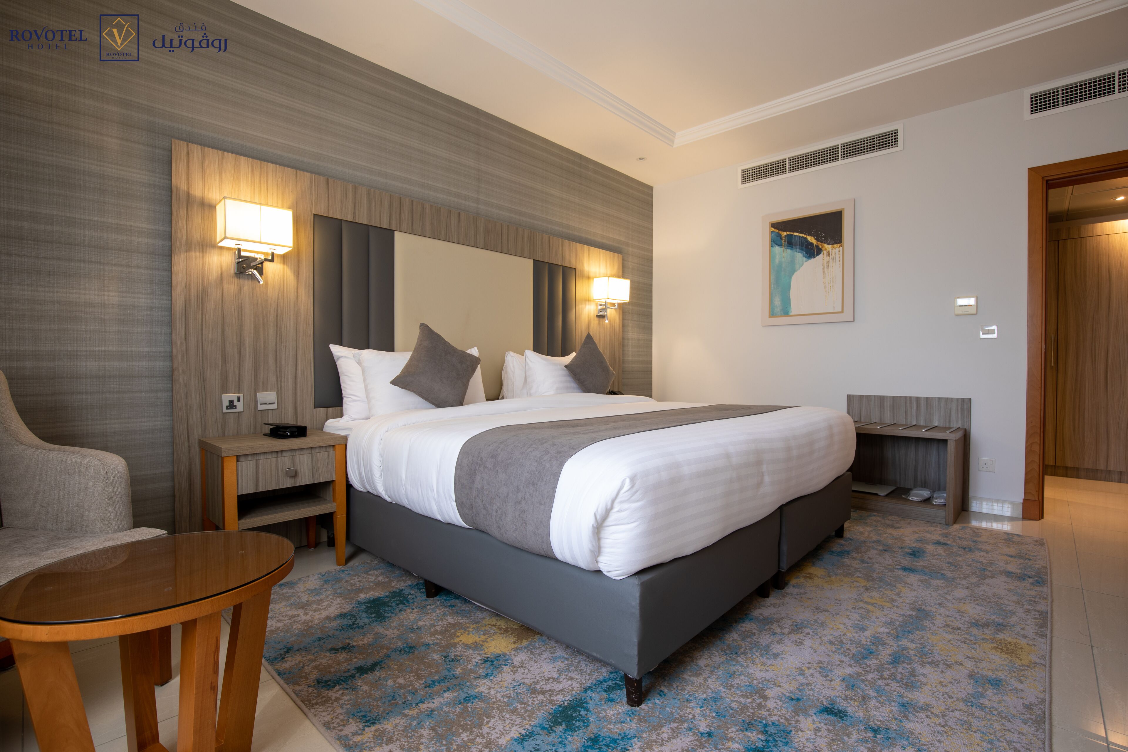 A modern hotel room with a large bed, bedside tables, a seating area, and a painting on the wall.