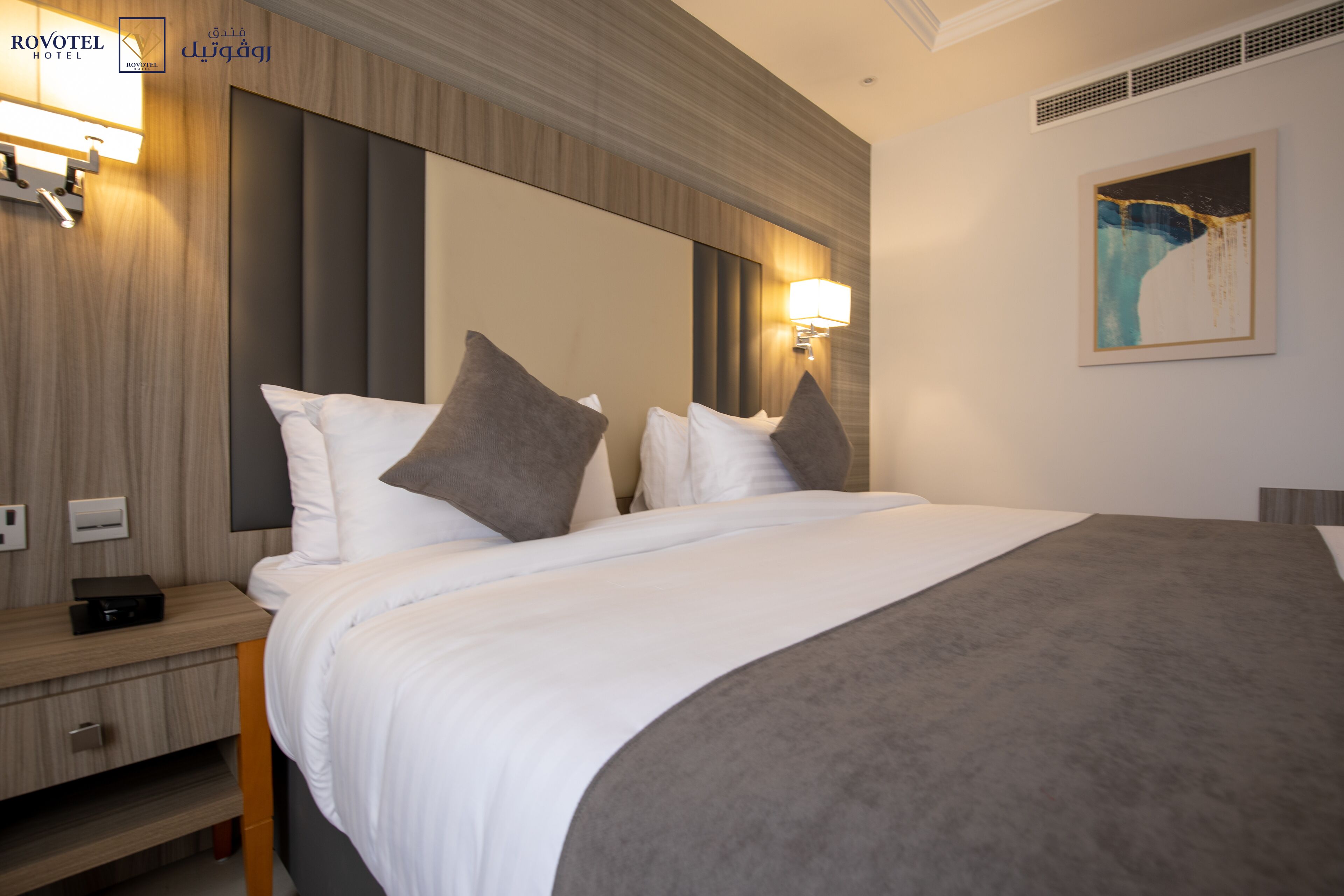 A hotel room with a large bed, two bedside lamps, a nightstand, and a painting on the wall.