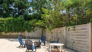 A sandy outdoor area with a wooden fence, a fire pit, and blue chairs. - Dunes Beach House 1 block from the ocean (Amagansett)