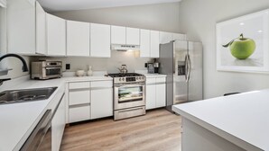 A modern kitchen with white cabinetry, stainless steel appliances, and a wooden floor. - Dunes Beach House 1 block from the ocean (Amagansett)