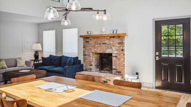 A modern living room with a fireplace, a dining area with a wooden table, and a sofa. - Dunes Beach House 1 block from the ocean (Amagansett)