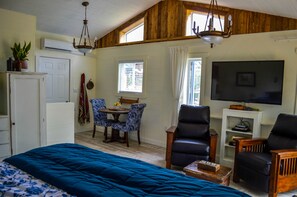 A room with a bed, a TV, a dining table with chairs, and a wooden ceiling.