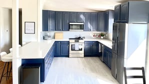 A modern kitchen with dark blue cabinets, stainless steel appliances, and a white countertop. - Large Home + Sleeps 20 + Hot Tub + Backyard Oasis + Optional add-on CABOOSE (Denver)