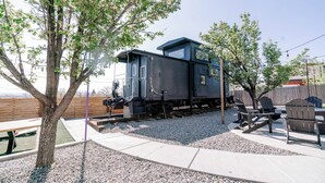 A train caboose with a small porch, surrounded by gravel and trees. - Large Home + Sleeps 20 + Hot Tub + Backyard Oasis + Optional add-on CABOOSE (Denver)