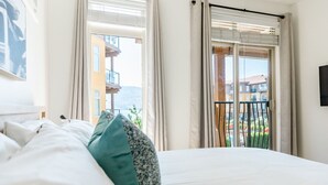 Ein Schlafzimmer mit einem großen Bett, einem Blick auf einen Balkon und einem Fenster mit Vorhängen.