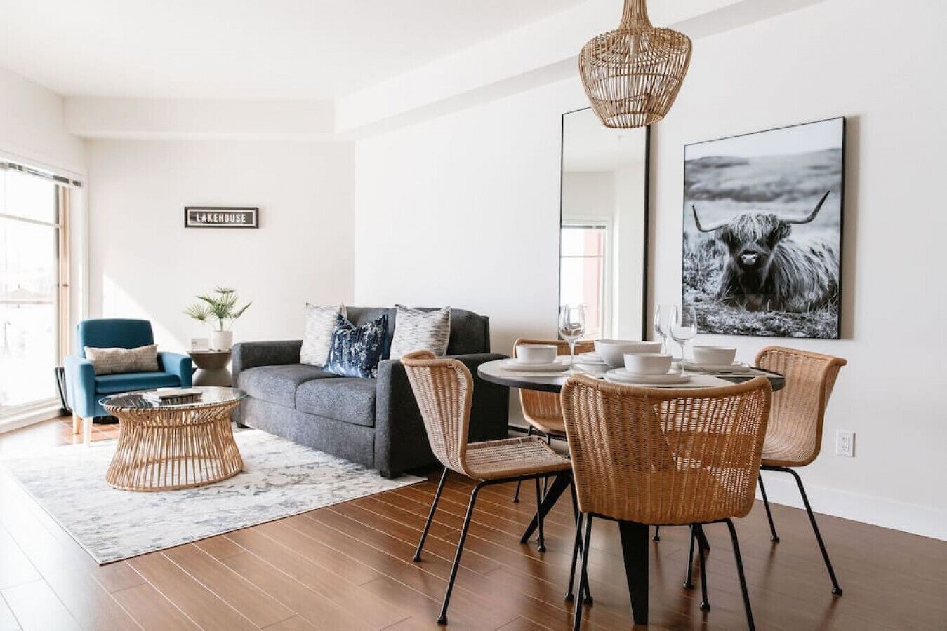 A modern living room with a sofa, dining table, wicker chairs, and a large mirror.