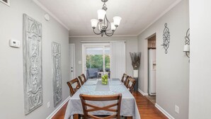 Une salle à manger avec une longue table, des chaises, un lustre, des panneaux décoratifs sur les murs et une vue par la fenêtre.