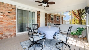 Une terrasse couverte avec une table et des chaises, un ventilateur de plafond et un mur en briques.