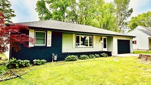 A single-story house with a dark exterior, a front garage, and a well-maintained lawn. - Stay just a short walk -0.3- miles from Lambeau! (Green Bay)