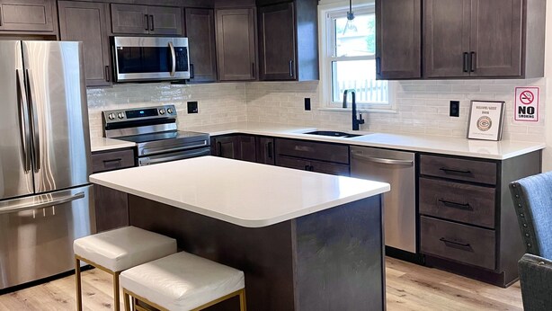 A modern kitchen with dark wood cabinets, stainless steel appliances, a large island with stools, and a no-smoking sign. - Stay just a short walk -0.3- miles from Lambeau! (Green Bay)