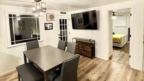 A dining area with a wooden table and chairs, a chandelier, a television mounted on the wall, and a bed visible through an open door. - Stay just a short walk -0.3- miles from Lambeau! (Green Bay)