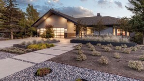 Uma casa moderna com telhado inclinado, garagem e jardim frontal ajardinado com caminhos de cascalho e arbustos pequenos.