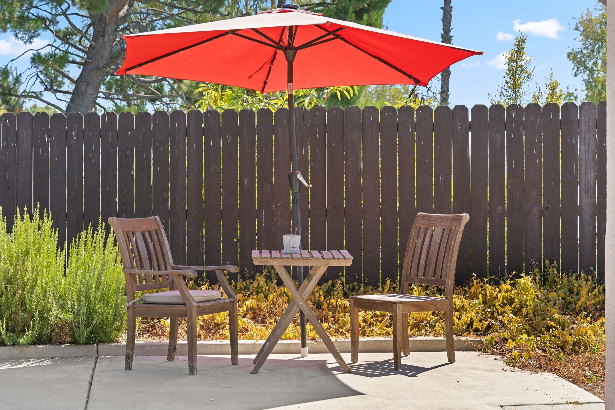 Une terrasse avec deux chaises en bois et une petite table, un parasol rouge et une clôture en bois en arrière-plan.