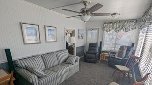 Un salon avec un canapé à rayures, un fauteuil inclinable, une chaise en bois, un ventilateur de plafond et un tapis à motifs.