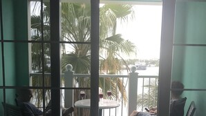 Een balkon met twee stoelen en een tafel, met uitzicht op een wateroppervlak en palmbomen.