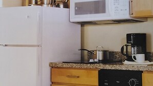 Een kleine keuken met een magnetron, koffiezetapparaat en vaatwasser. Er is een eettafel met stoelen.
