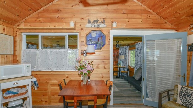 L’intérieur d’un chalet en bois comprend une table à manger, des chaises, un four à micro-ondes et une pancarte de bienvenue.