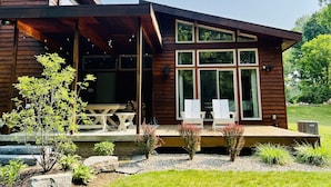 Ein modernes Holzhaus mit einer überdachten Veranda, großen Fenstern und Sitzgelegenheiten im Freien.