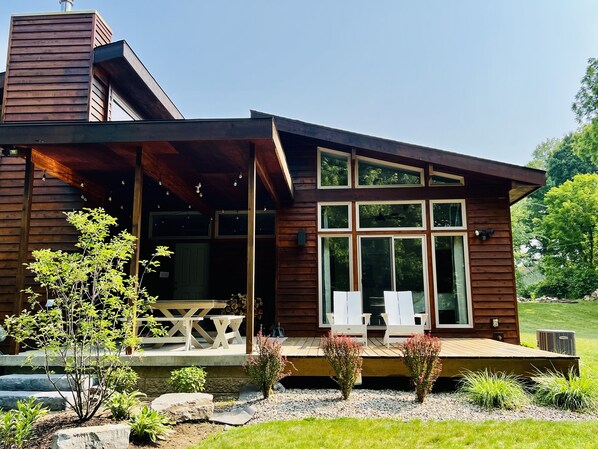 A modern wooden house with a covered porch, large windows, and outdoor seating.