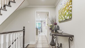 Ein Flur mit einer Treppe, einem Konsolentisch mit Vase und Schale sowie einem großen abstrakten Gemälde an der Wand.
