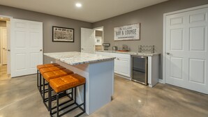 Une cuisine moderne avec un plan de travail en marbre, des tabourets de bar en bois et un réfrigérateur.