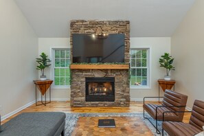 A living room with a stone fireplace, two windows, a sofa, and a rug.