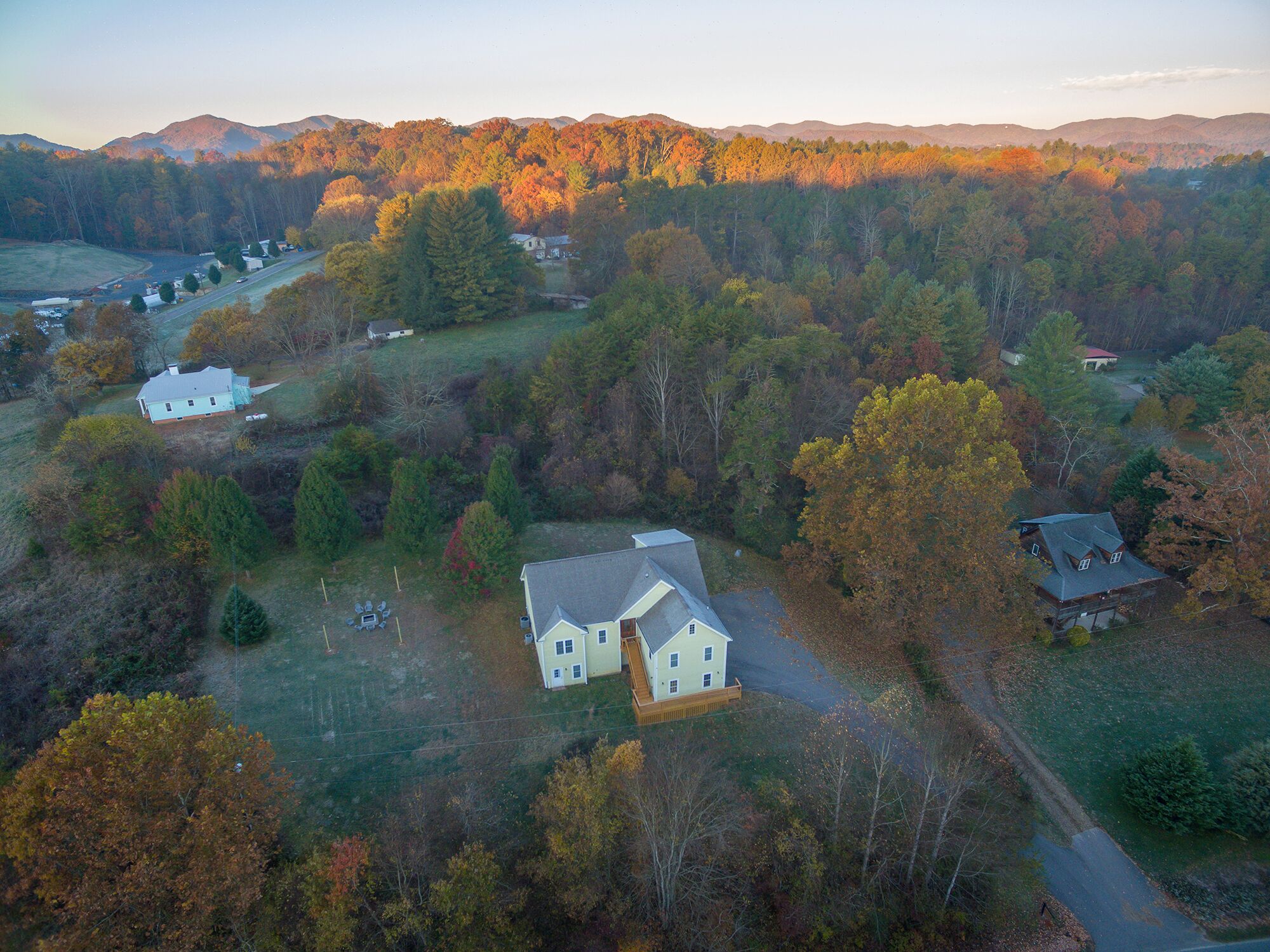 An aerial view of a rural area with several houses surrounded by dense forests and rolling hills.