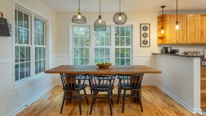 Une cuisine avec une table en bois, quatre chaises, des luminaires suspendus et des armoires en bois.