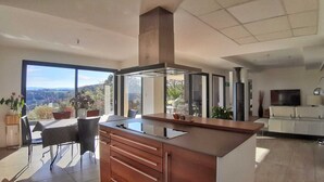 A modern kitchen with a large island, a dining area with a view, and a living room with a TV. - CONTEMPORARY VILLA WITH AMAZING VIEW OF LAKE SALAGOU (Soumont)