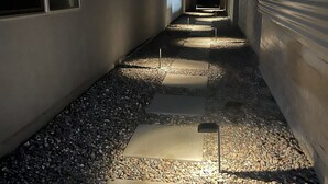 En smal gång med stenar som fungerar som steg, som leder fram till ett garage, omgivet av murar och en mörk himmel.