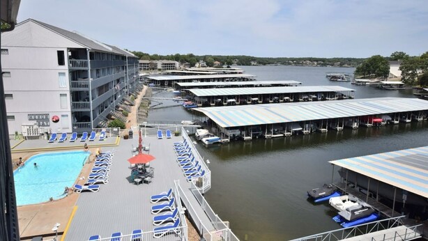 A marina with docked boats, a swimming pool with sun loungers, and a multi-story building with balconies.