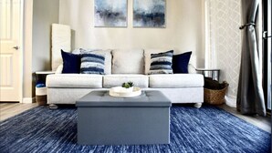 A modern living room with a grey sofa, blue and white cushions, a grey ottoman, and two abstract paintings on the wall.
