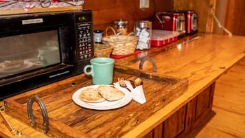 A wooden kitchen counter with a microwave, a tray with bread and a mug, and a basket in the background.