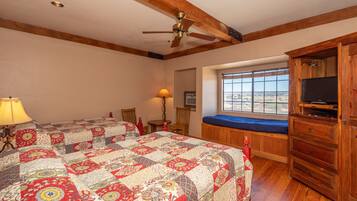Un dormitorio con una cama grande, vigas de techo de madera, un ventilador de techo, un ventanal con vistas y un mueble para televisión.