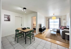 A living room with a sofa, a coffee table, and a TV. There is a dining area with a table and chairs.