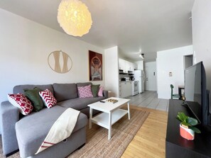 A modern living room with a grey sofa, white coffee table, and a television on a black stand. - Beautiful apartment in the lower town (Québec)