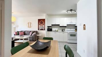 Une cuisine moderne avec des meubles blancs, un four à micro-ondes et un four traditionnel. On y trouve également un coin repas avec une table en bois et des chaises vertes.