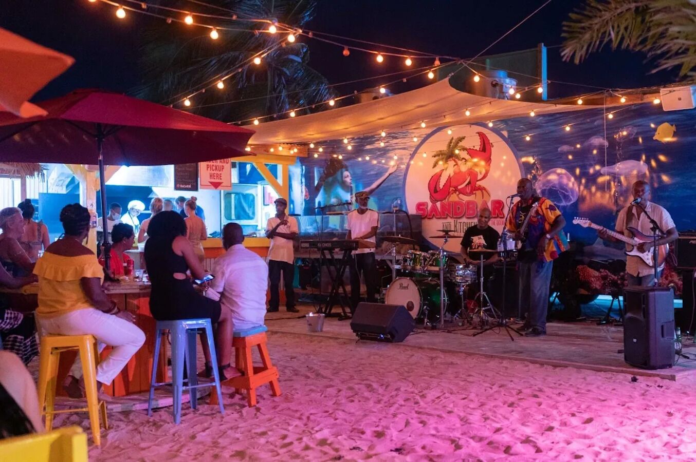 Eine Strandbar mit Bühne für Live-Musik, Außenbereich zum Sitzen und einem Schild für die Abholzone.