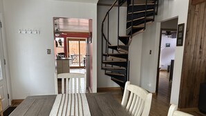 Un comedor con una mesa de madera, sillas y un cuenco decorativo. Se observa una escalera de caracol al fondo.