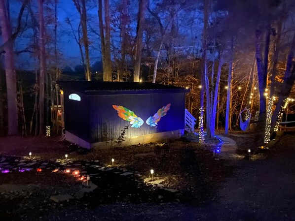 A cabin with a colorful bird mural, surrounded by trees and string lights. - Mosaic Villa-Riverfront Retreat for Two-Downtown (Sparta)