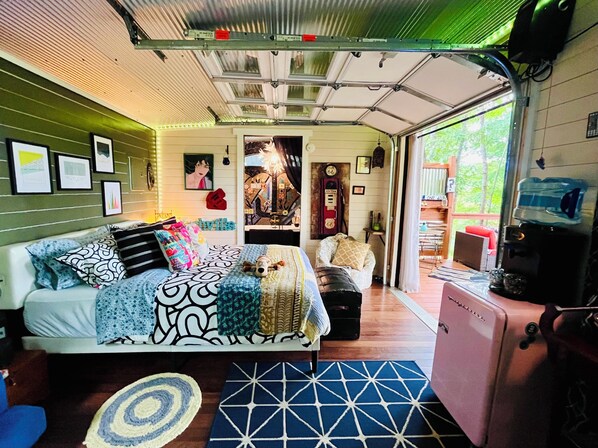 Una habitación compacta y bien iluminada con una cama, un pequeño rincón de descanso y una kitchenette.